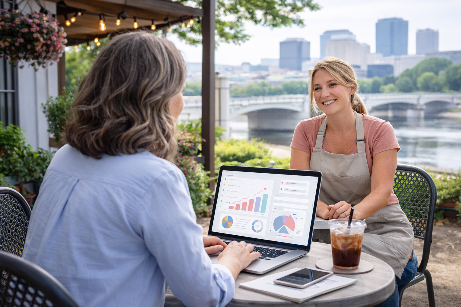 A woman working on a laptop outdoors with a small business owner, reviewing website analytics and strategy with the Dayton skyline in the background, representing website help and support for local businesses